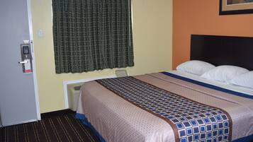 Habitación de hotel con cama, puerta, ventana con cortinas y un conducto de ventilación en la pared.