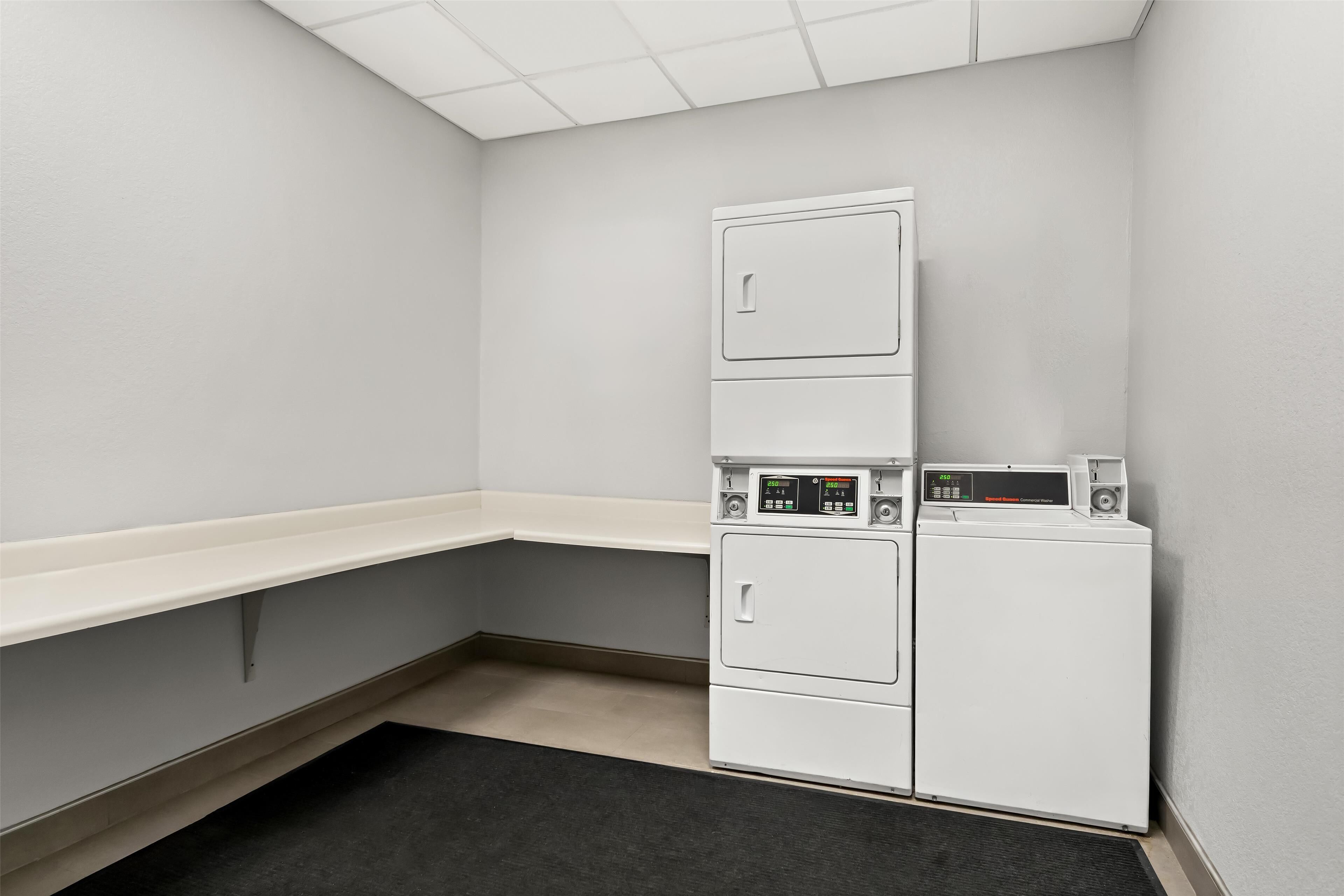 A laundry room with a stacked washer and dryer, a bench, and a black rug.