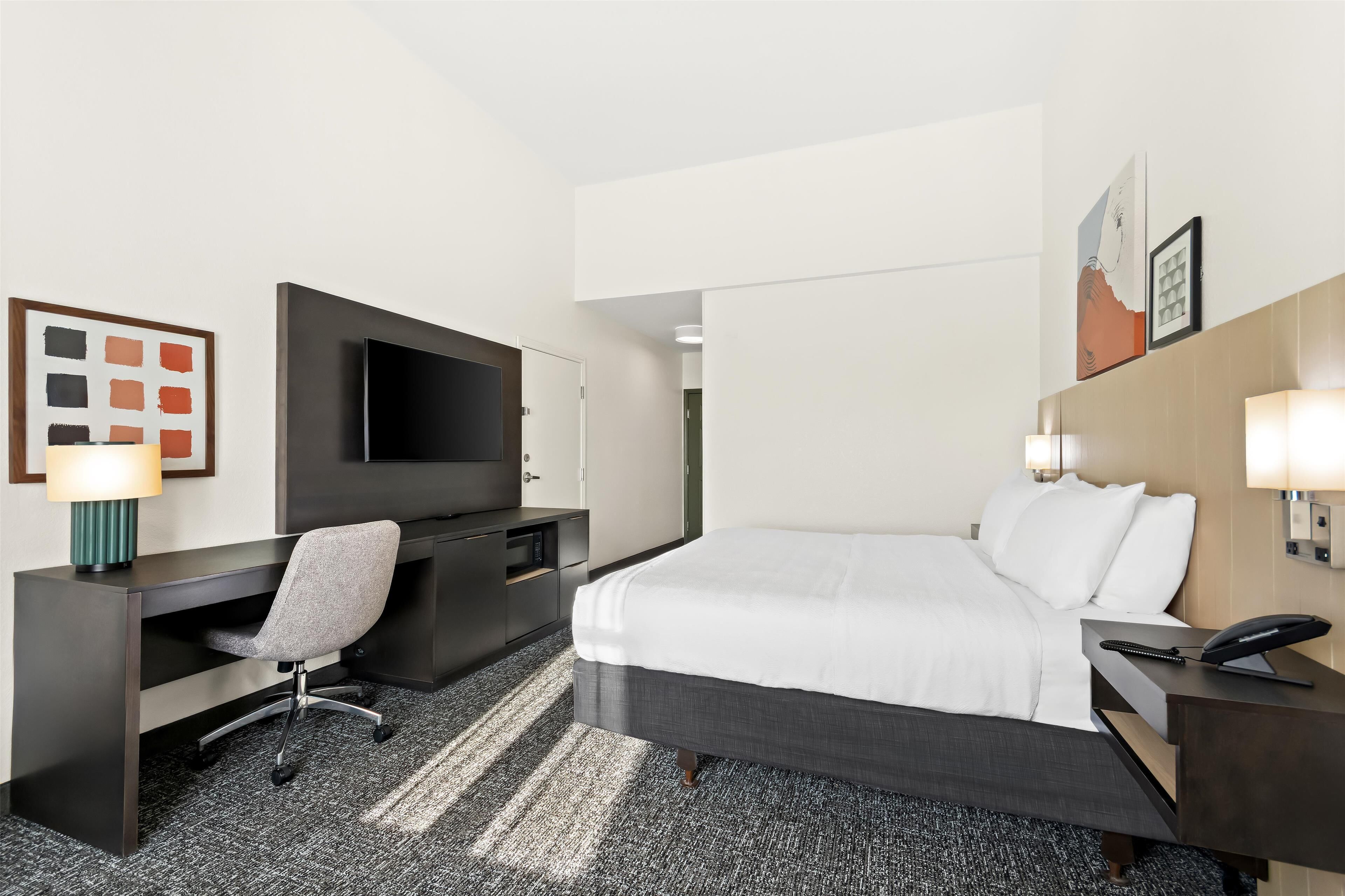 A hotel room with a bed, desk, chair, TV, and artwork on the walls.