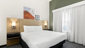 A hotel room with a large bed, two bedside tables, a wall-mounted artwork, and a window with sheer curtains.