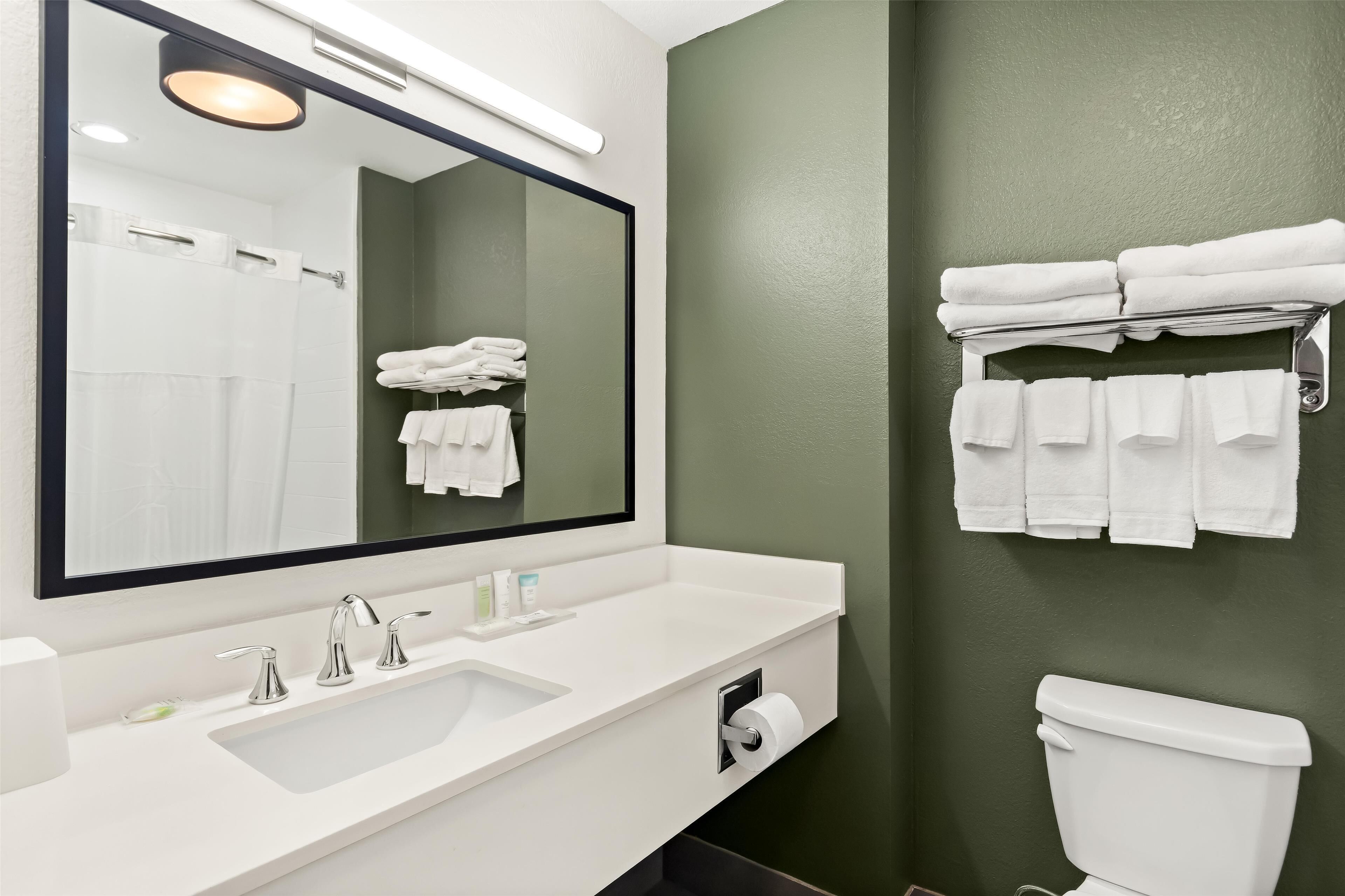 A bathroom with a white sink, a large mirror, and a toilet. There are towels hanging on a rack above the toilet.