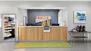 A reception area with a wooden reception desk, a green rug, and a wall with abstract art. - Spark by Hilton Panama City Beach (Panama City Beach)
