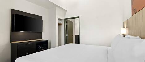 A hotel room with a large bed, a flat-screen TV, a dresser, and a mirror.