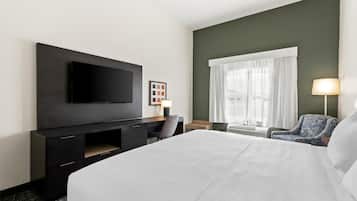 Une chambre d’hôtel dotée d’un grand lit, d’un téléviseur à écran plat fixé au mur, d’un bureau avec une chaise, d’une fenêtre avec des rideaux et d’une lampe.