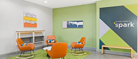 A modern office space with orange rocking chairs, a green carpet, and a wooden bench.