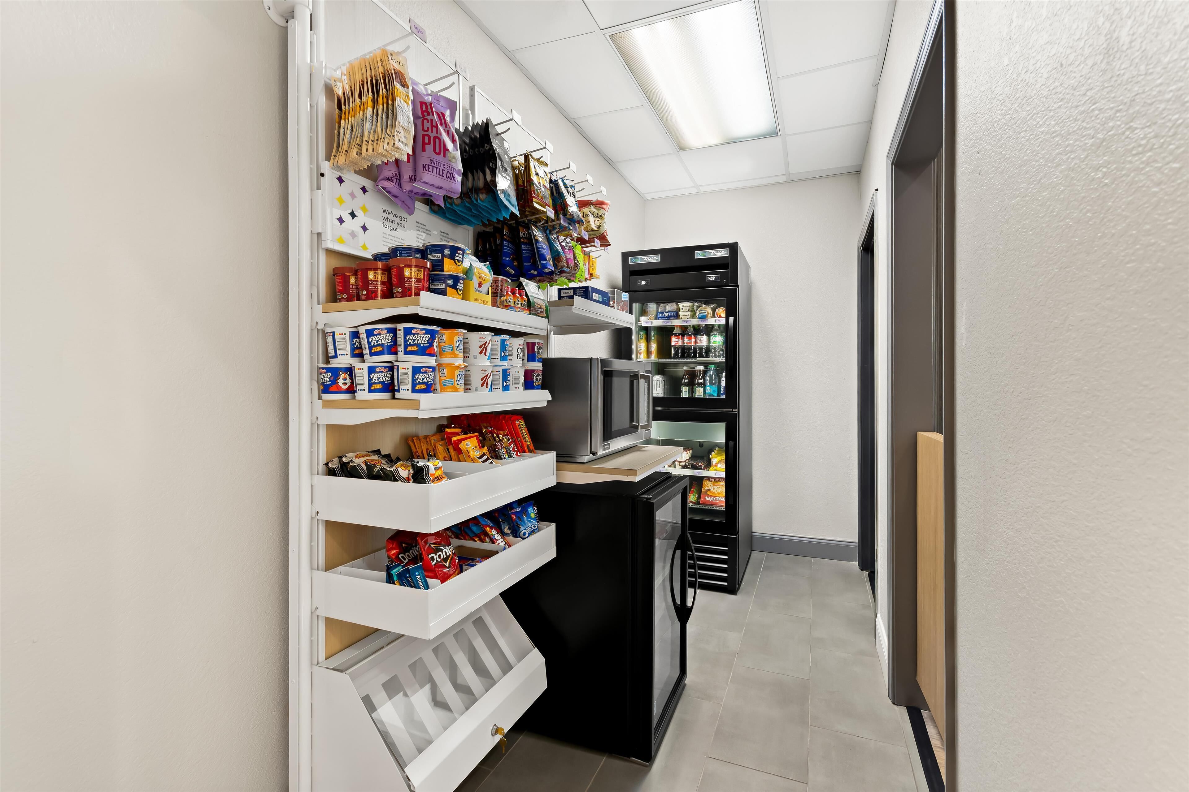 Een smalle gang met planken vol snacks en drankjes, een koelkast en een automaat.