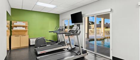 A fitness center with treadmills, a mirrored wall, a television, and a pool view.