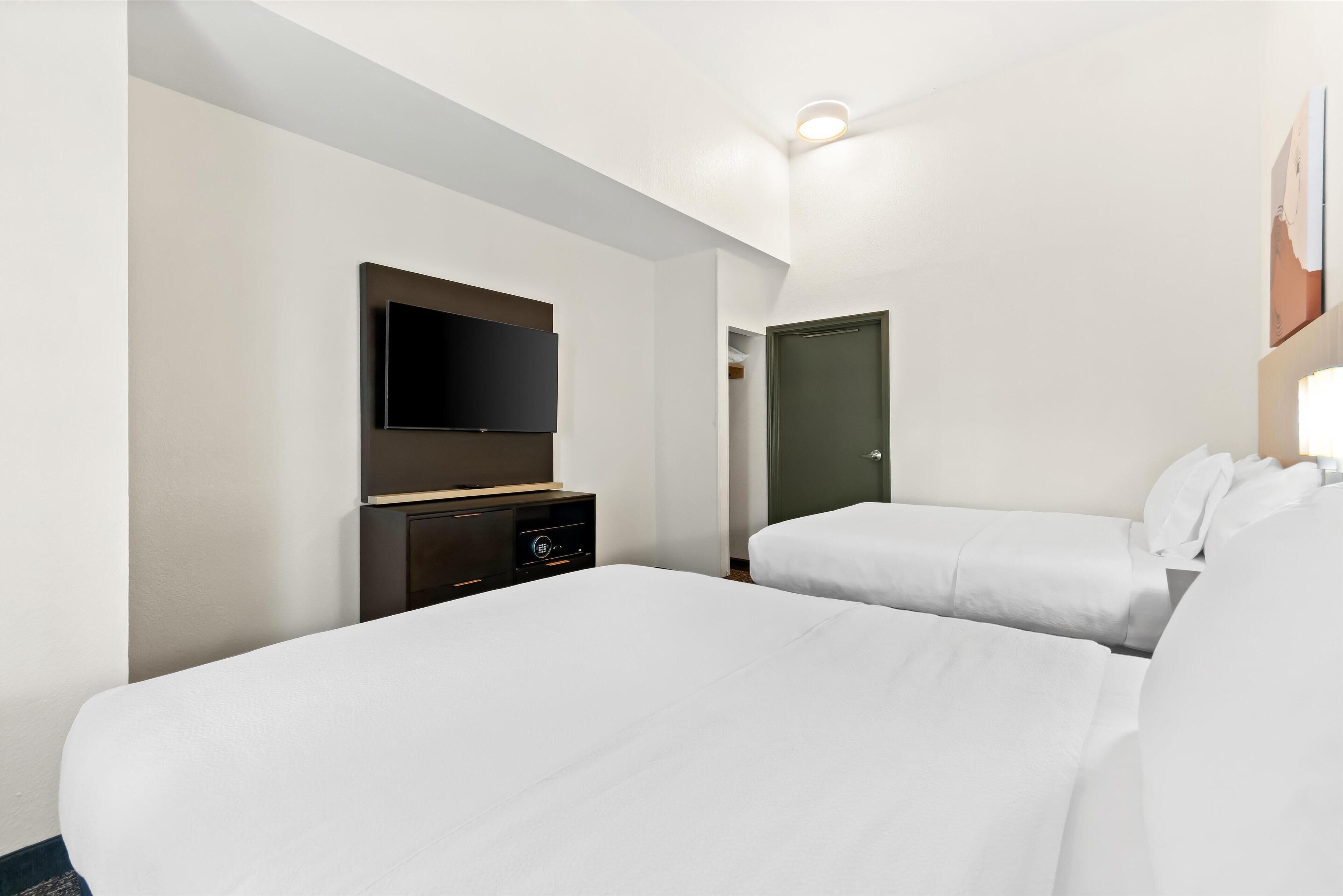 A hotel room with two beds, a flat-screen TV, a dresser, and a door.