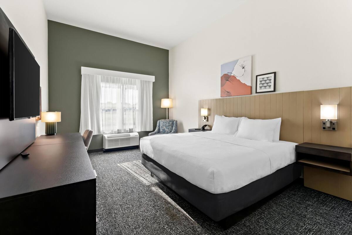 Quarto de hotel com uma cama grande, uma escrivaninha, uma cadeira, uma televisão e uma janela com cortinas.