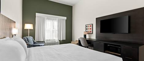 A hotel room with a large bed, a desk with a flat-screen TV, a chair, and a window with curtains.