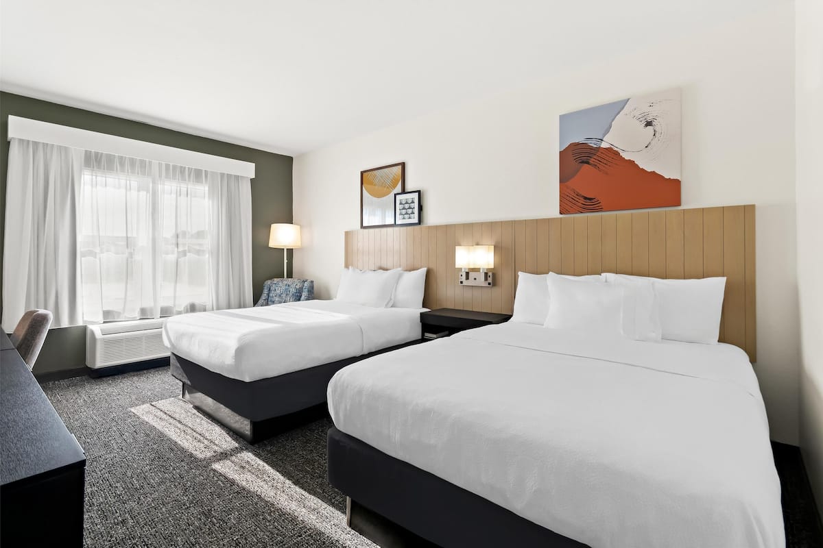 Quarto de hotel com duas camas, uma escrivaninha e uma janela grande com cortinas.