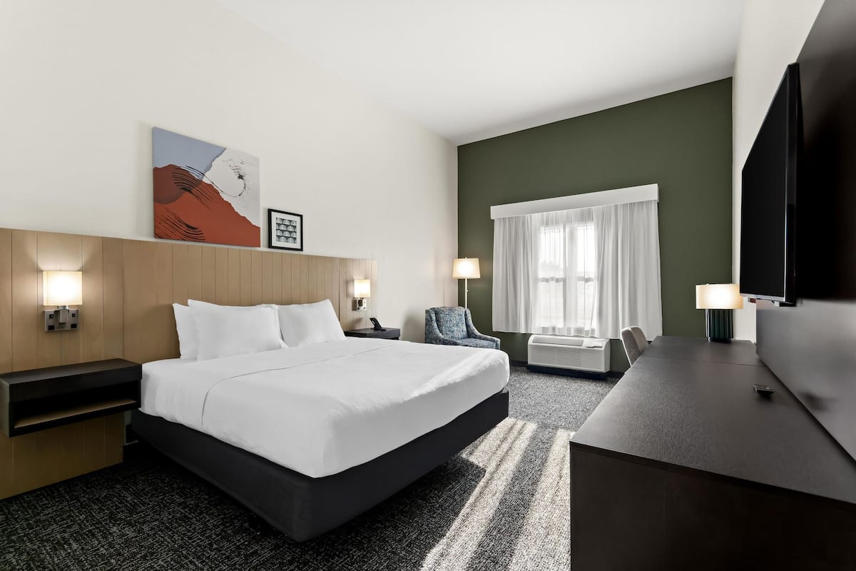 Quarto de hotel com uma cama grande, uma escrivaninha, uma cadeira, televisão e obras de arte na parede.