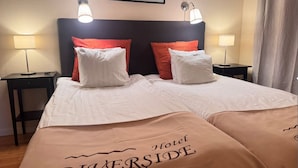Una camera d'albergo con un letto, due lampade ai comodini, una testiera e un quadro appeso al muro.