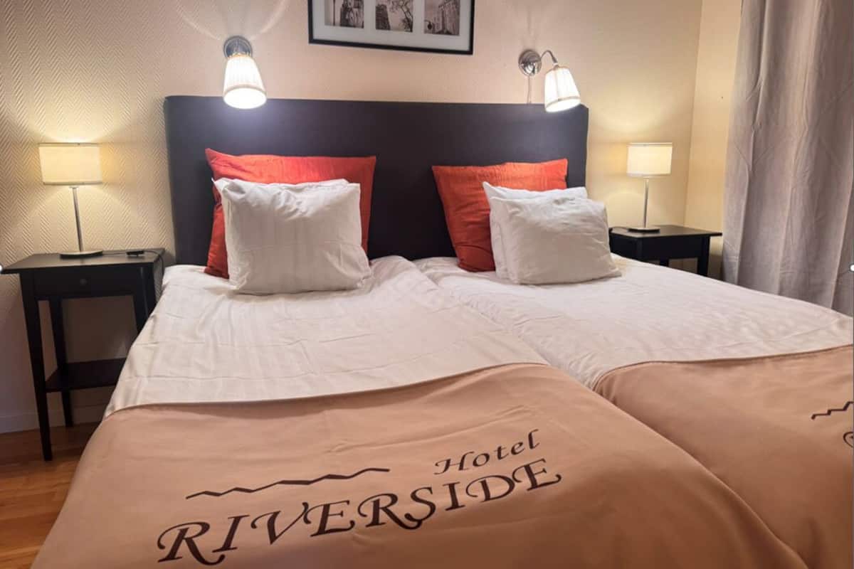 A hotel room with a bed, two bedside lamps, a headboard, and a framed picture on the wall.