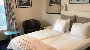 A hotel room with a bed, a chair, a small table, and framed pictures on the wall.