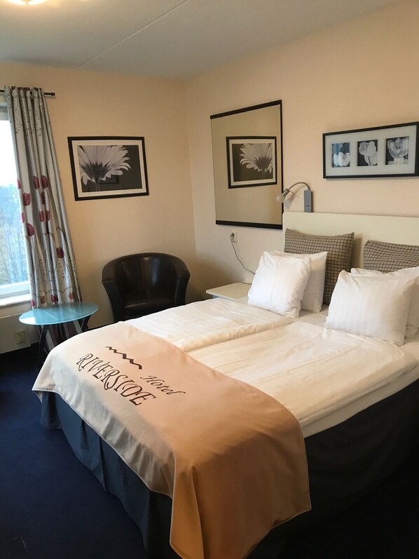 A hotel room with a bed, a chair, a small table, and framed pictures on the wall.