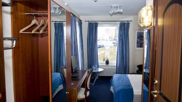 A hotel room with a bed, a desk with a chair, a wardrobe, and a window with curtains.