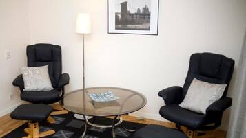 Una habitación con dos sillas negras, una mesa de vidrio, una lámpara y un cuadro en la pared.
