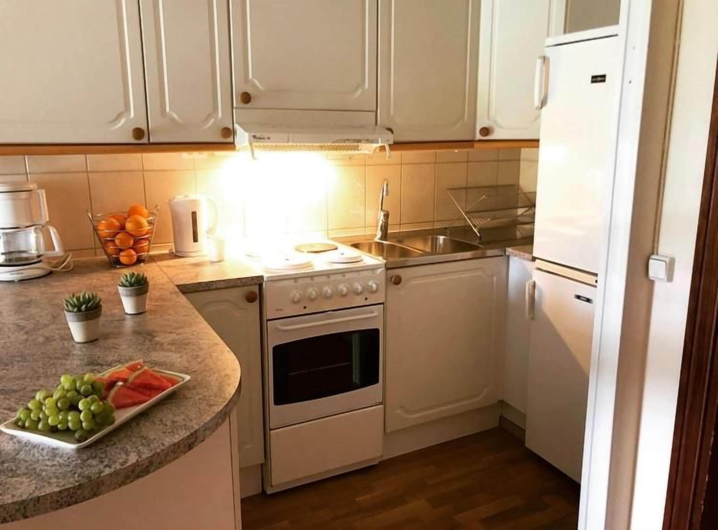Una cocina compacta con armarios blancos, una encimera con un frutero, una cafetera y un lavabo.