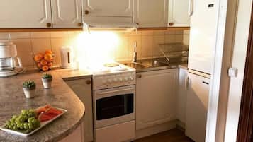 Una cocina compacta con armarios blancos, una encimera con un frutero, una cafetera y un lavabo.