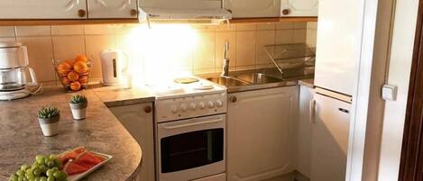 A compact kitchen with white cabinets, a countertop with a fruit bowl, a coffee maker, and a sink.