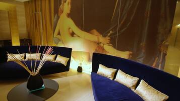 A modern hotel room with a large wall mural, a blue sofa, a small round table with a vase, and a decorative wall panel.