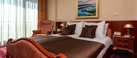 A hotel room with a large bed, a chair, a nightstand, and a painting on the wall.