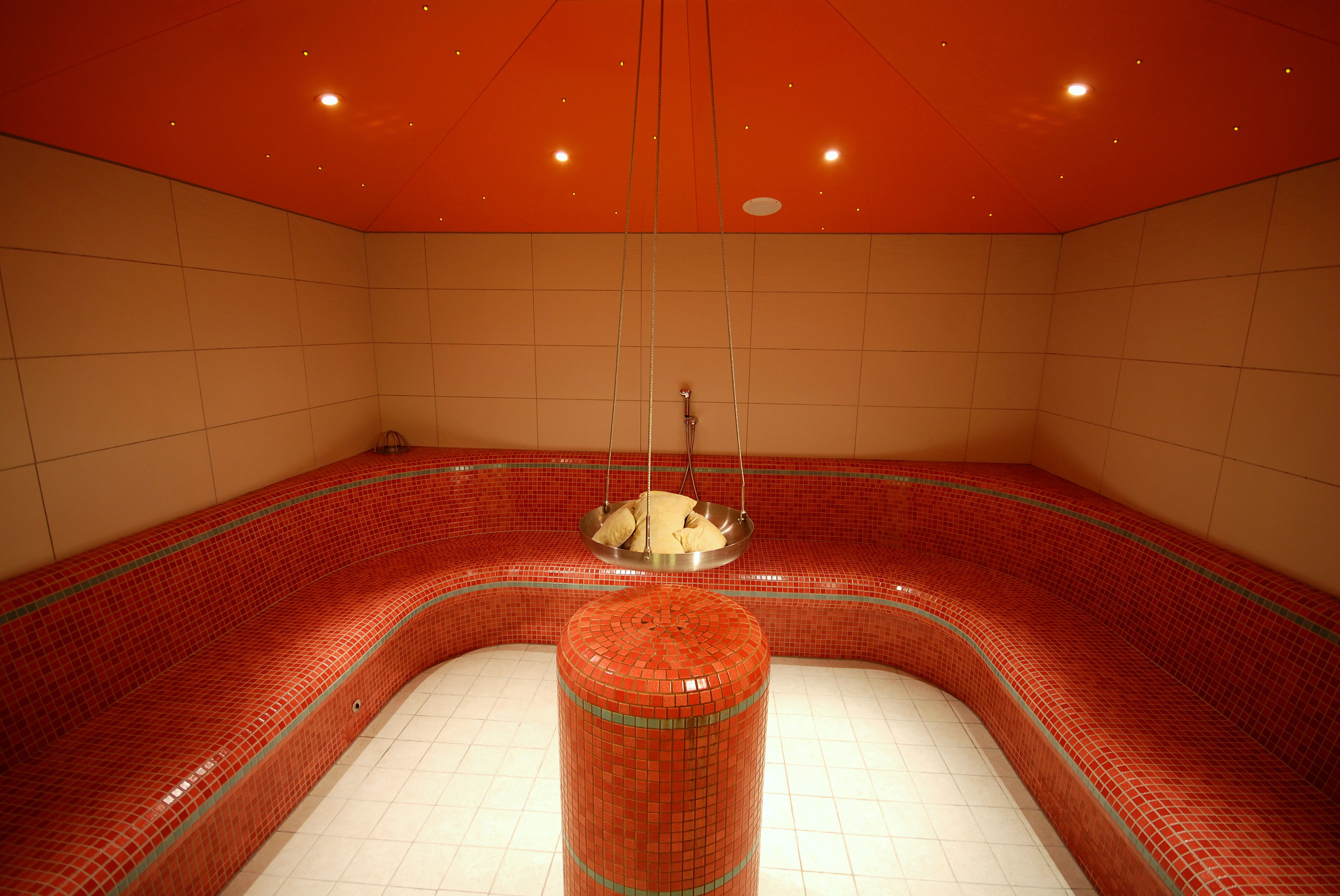 A red-tiled spa area with a central column and hanging showerhead.