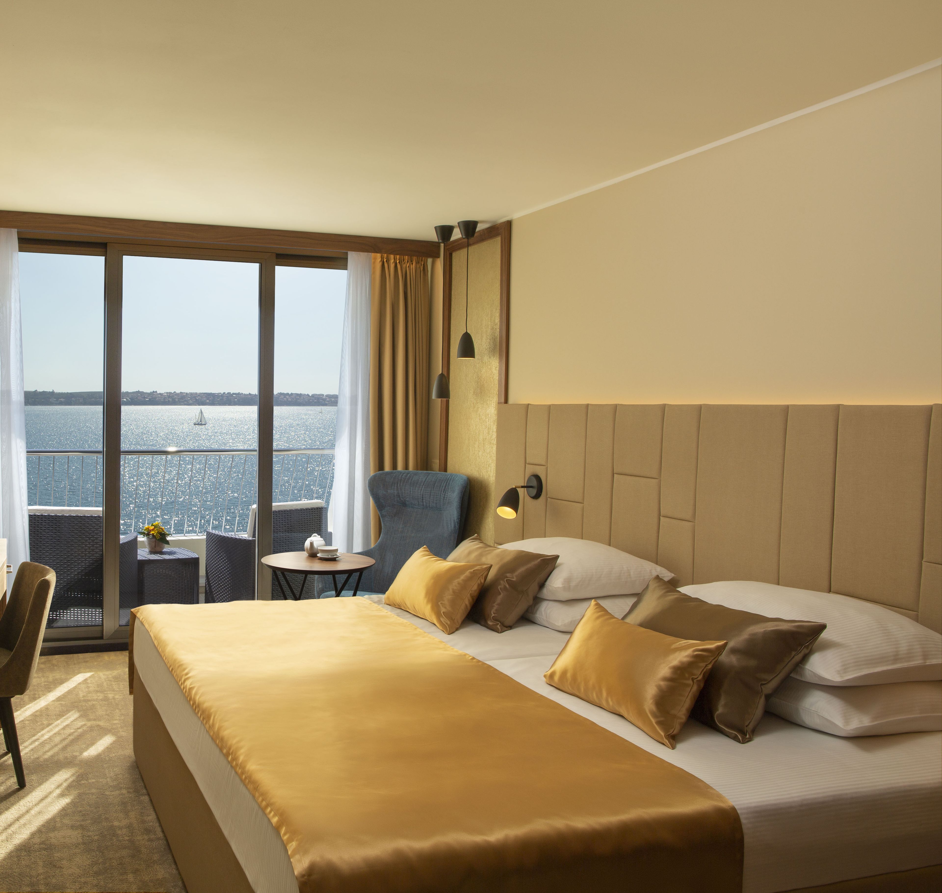 A hotel room with a large bed, a chair, a small table, and a view of the water.