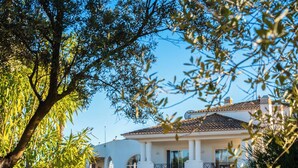A two-story building with a white facade and a tiled roof, surrounded by greenery and trees. - Colina Verde Resort (Olhao)