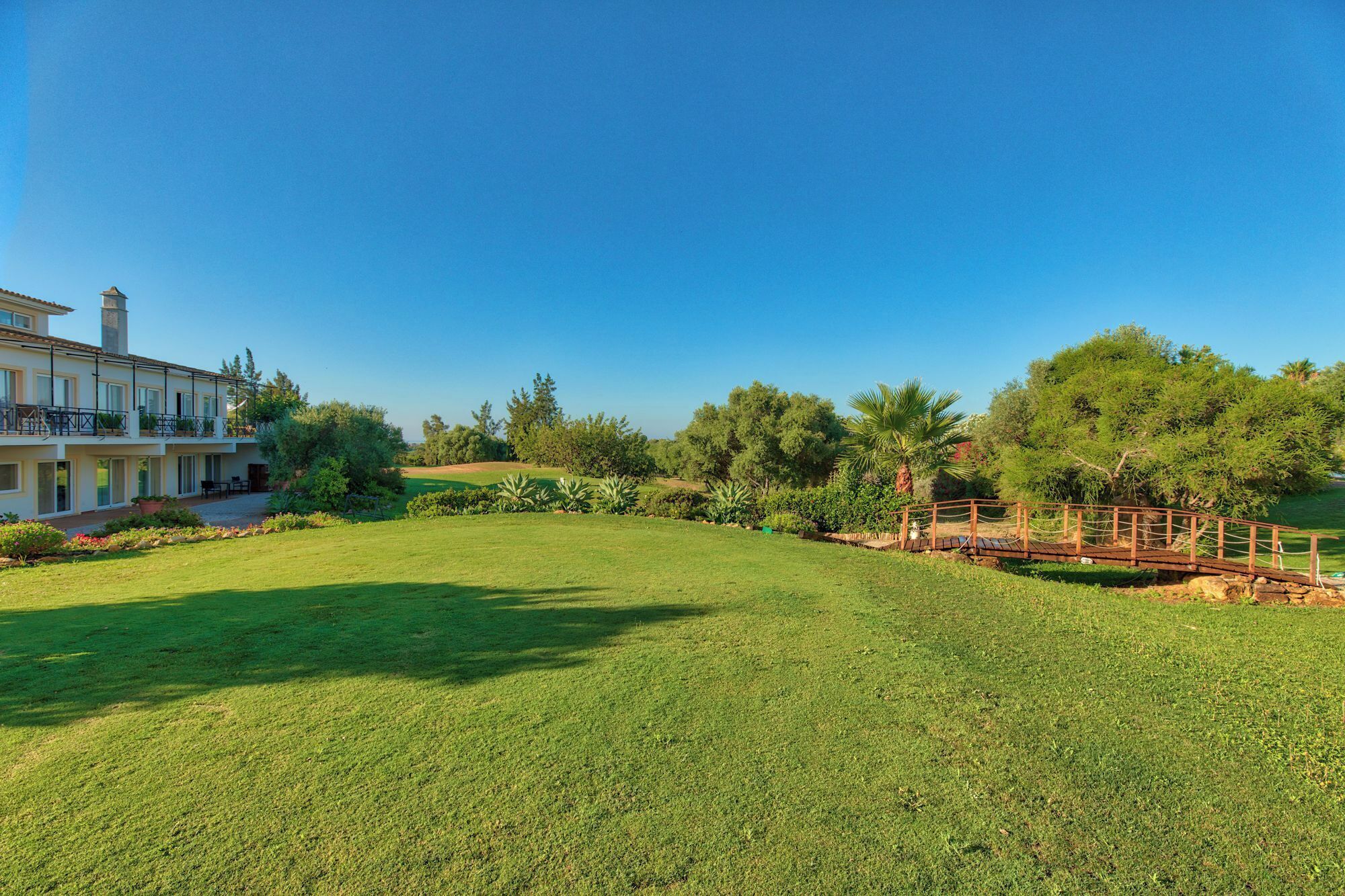 A large, well-maintained lawn with a wooden bridge and a two-story building with balconies.