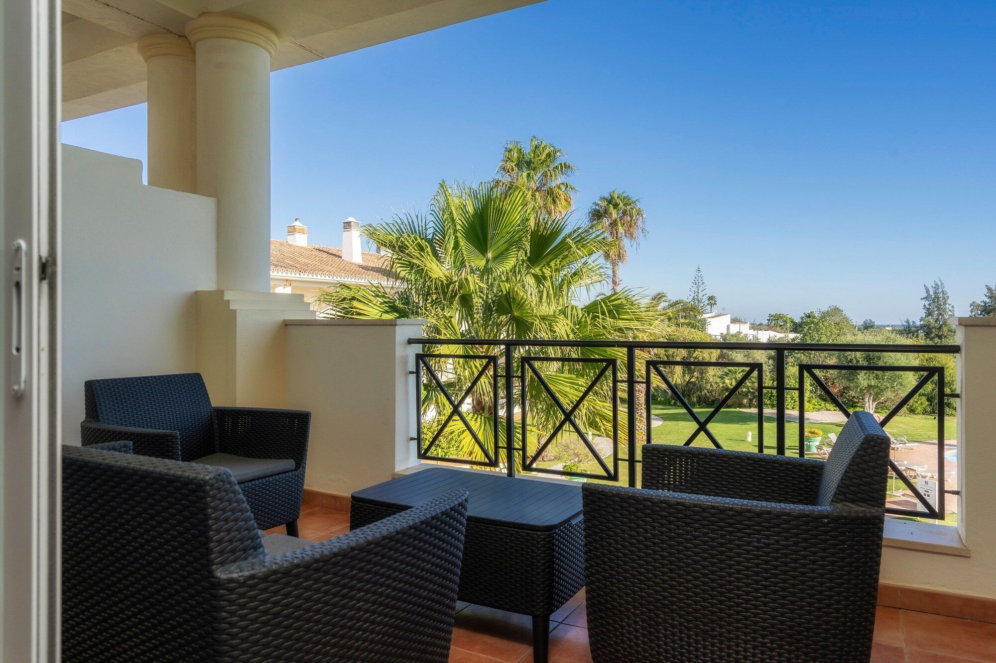 A balcony with wicker furniture, a view of palm trees, and a clear sky.