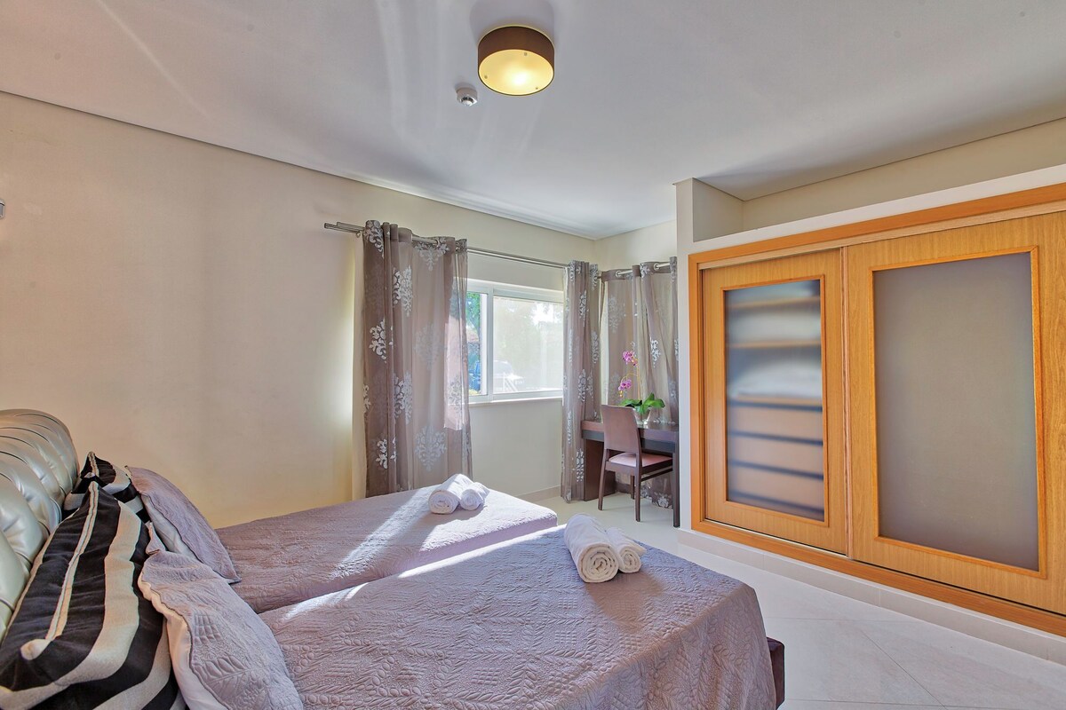A bedroom with a bed, a chair, a desk, and a wardrobe.