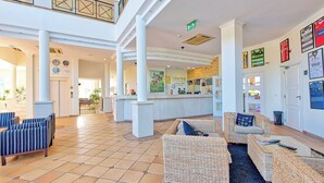 A spacious lobby with a reception desk, wicker furniture, and a tiled floor. - Colina Verde Resort (Olhao)