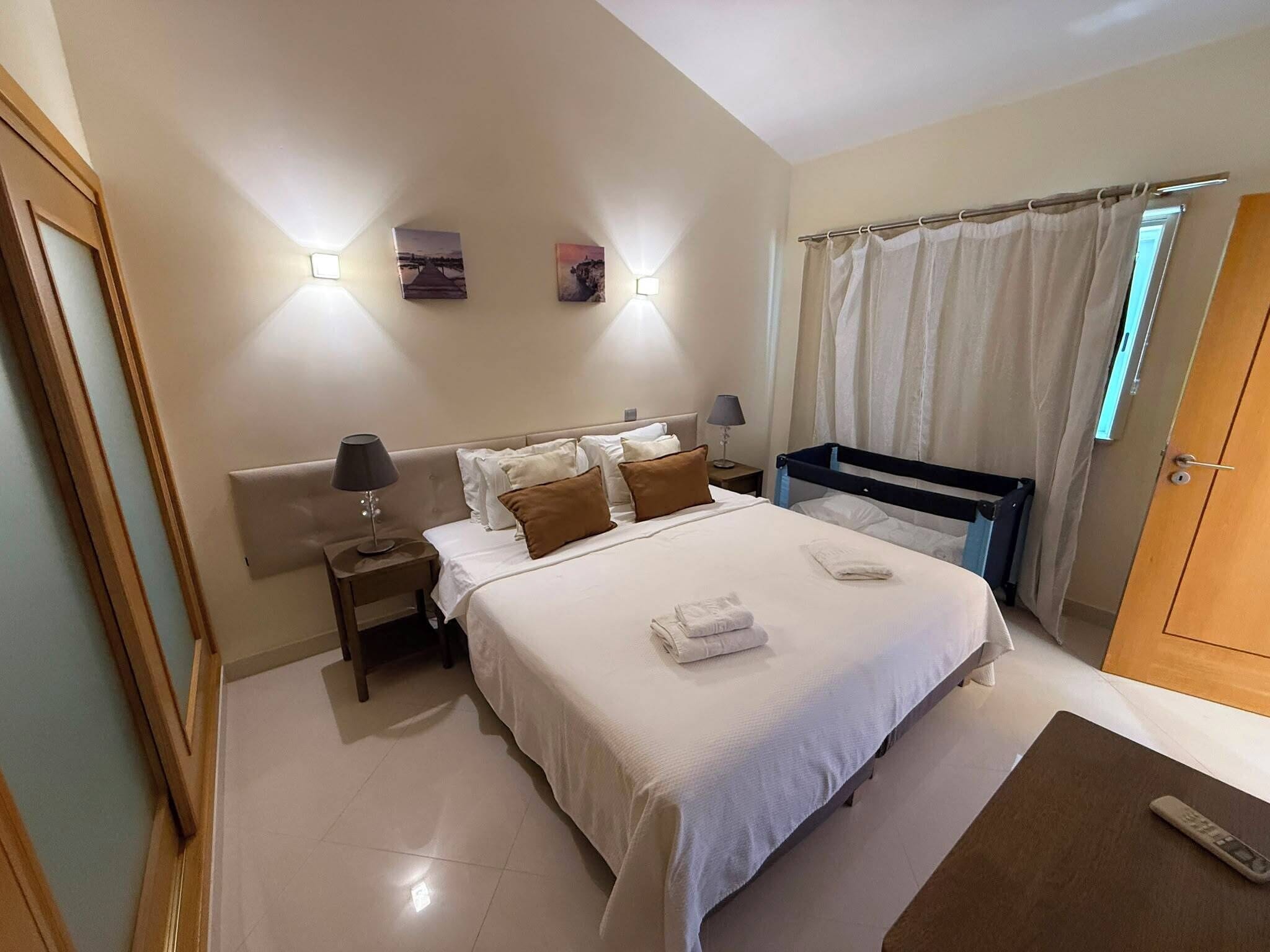 Una habitación de hotel con una cama, mesitas de noche, una lámpara, una ventana con cortinas y una puerta.