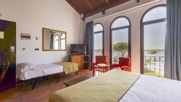 Habitación de hotel con dos camas, televisión, escritorio y ventanas amplias con vistas.