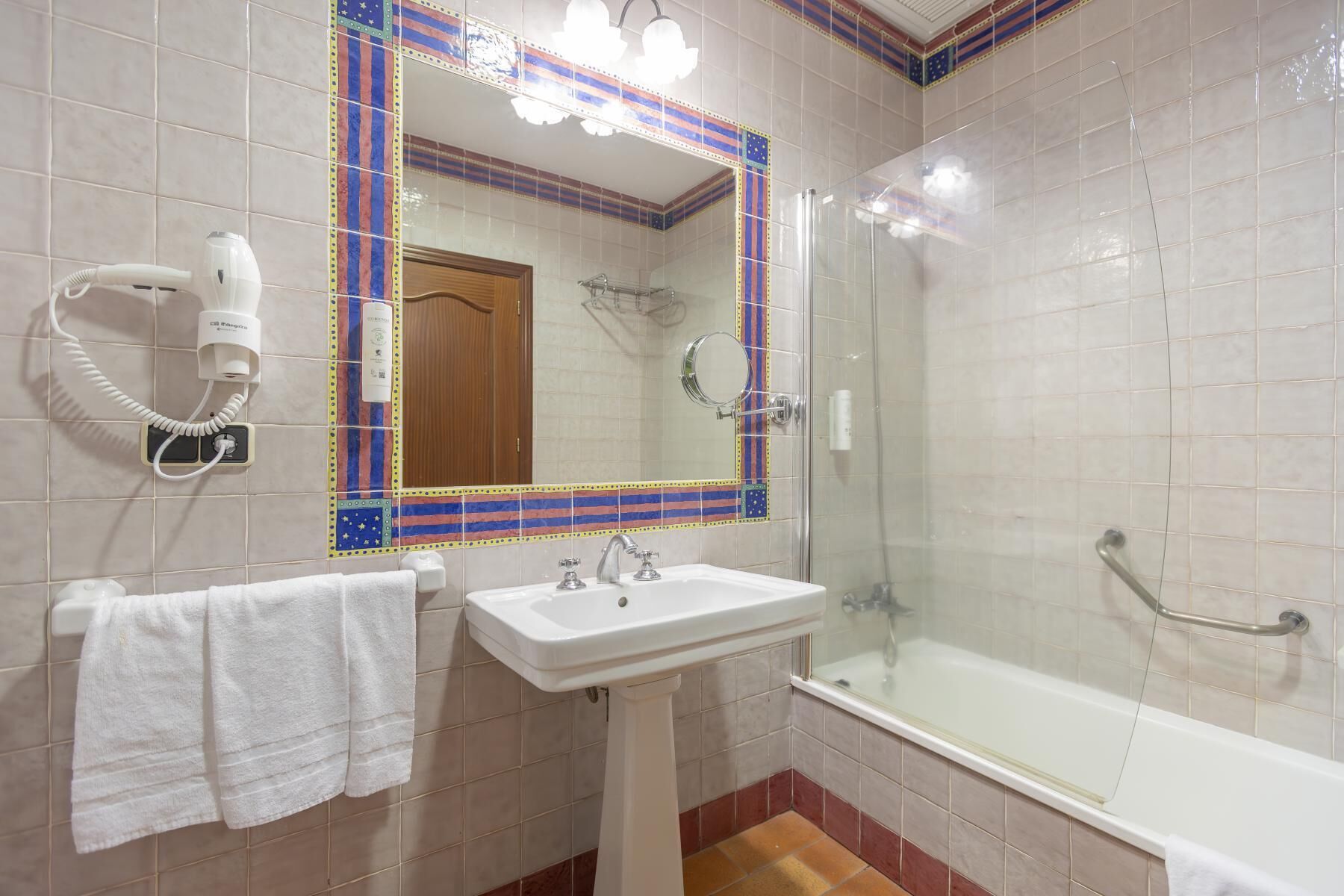 A bathroom with a white sink, a mirror, a hairdryer, and a glass-enclosed shower.