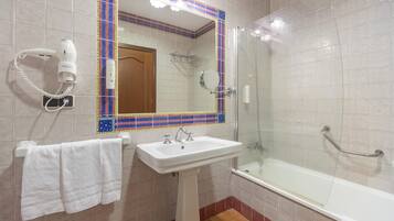 A bathroom with a white sink, a mirror, a hairdryer, and a glass-enclosed shower.