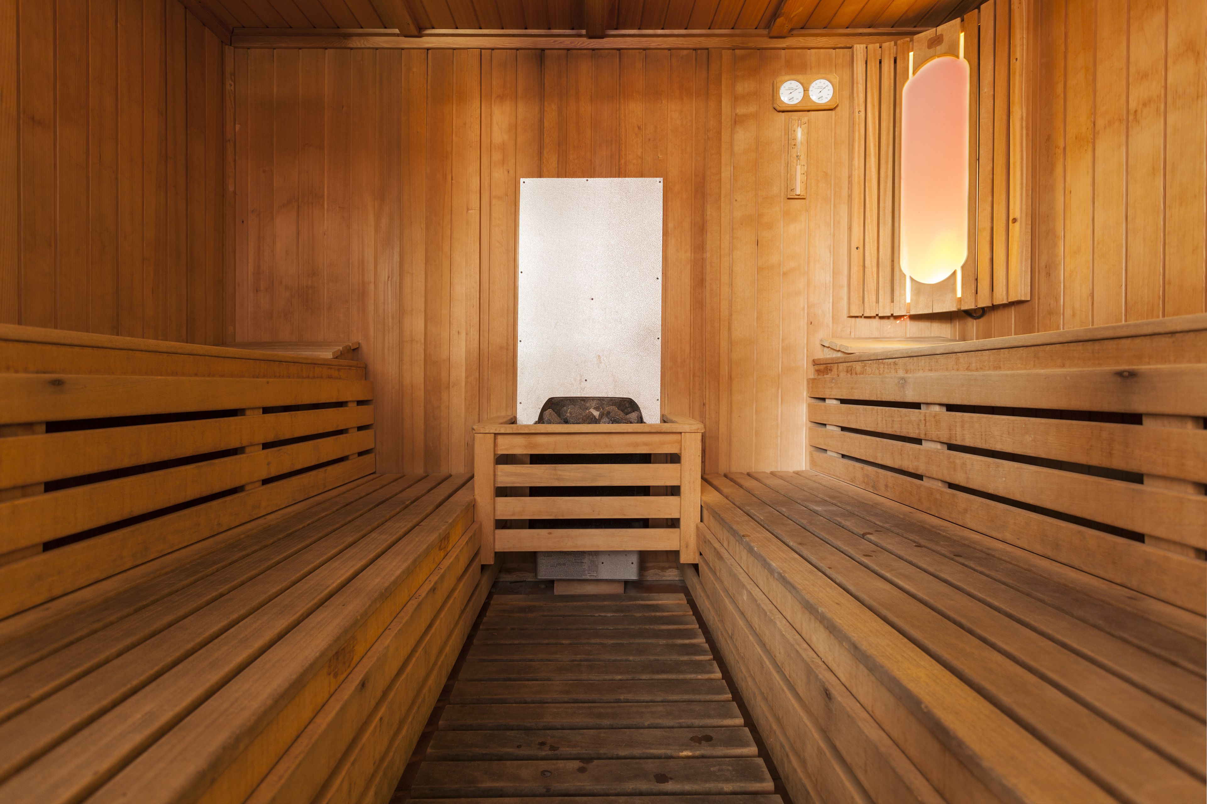 Een houten sauna met banken aan weerszijden en een bank in het midden, met een wandlamp.