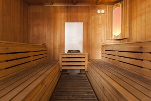 Een houten sauna met banken aan weerszijden en een bank in het midden, met een wandlamp.