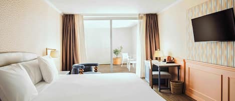 Ein Hotelzimmer mit einem großen Bett, einem Schreibtisch mit Stuhl, einem Fernseher und Blick ins Freie.