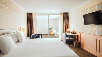 Een hotelkamer met een groot bed, een bureau met stoel, een televisie en uitzicht op het omliggende landschap.