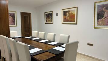 A conference room with a long wooden table, six white chairs, and framed artworks on the walls.