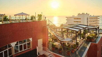 A rooftop terrace with a glass balustrade, outdoor seating, and potted plants.
