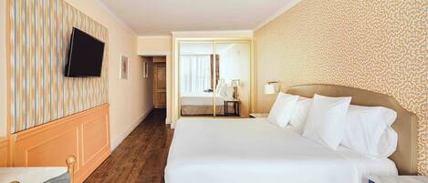 A hotel room with a large bed, a television mounted on the wall, a wooden floor, and a patterned wallpaper on one wall.
