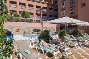 A poolside area with lounge chairs, umbrellas, and a stone wall.