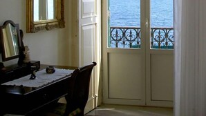 A room with a large window overlooking the sea, a television mounted on the wall, and a table with a chair. - Hotel Aurora (Syracuse)