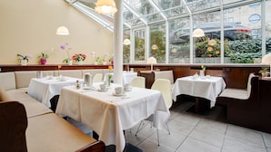 Un restaurante con mesas cubiertas con manteles blancos, cabinas acolchadas y lámparas colgantes.