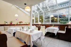 A restaurant with white tablecloth-covered tables, cushioned booths, and hanging pendant lights.