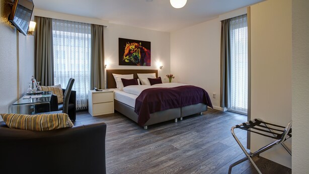 Una habitación de hotel moderna con cama, escritorio, silla, televisor y ventana con cortinas.